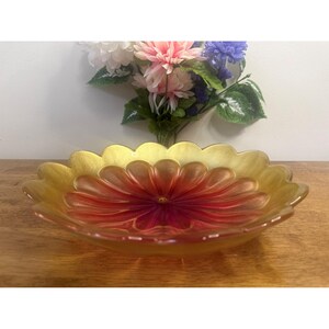 May include: A decorative glass bowl with a flower design. The bowl has a gold rim and a red and orange centre, resembling a flower. The bowl is on a wooden surface.