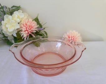 May include: A pink glass bowl with two handles. The bowl has a textured design and is made of clear glass.