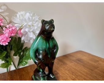 May include: A ceramic bear figurine with a glossy finish. The bear has a dark brown head and legs, with a vibrant green and brown body. The figurine is standing upright and has a detailed, textured appearance. The bear is a decorative item.