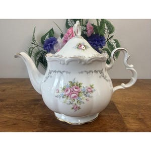 Peut inclure: Théière en porcelaine blanche avec couvercle, ornée de roses roses et d'accents bleus. La théière a un bec courbé, une poignée ornée et une bordure dorée. Une pièce décorative pour servir le thé.
