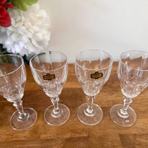 May include: Four clear glass stemmed shot glasses with a cut crystal design. Each glass has a gold label with the word "Cristal" printed on it.