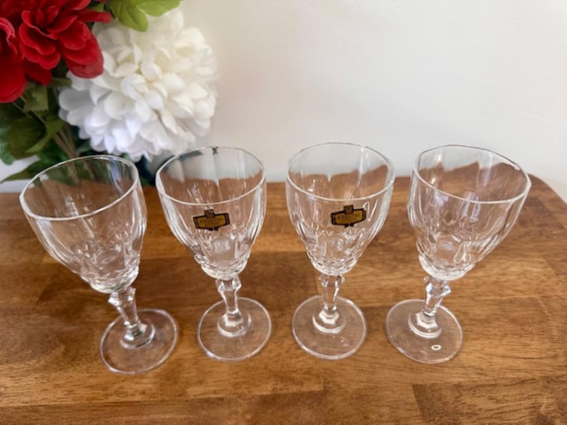 May include: Four clear glass stemmed shot glasses with a cut crystal design. Each glass has a gold label with the word "Cristal" printed on it.