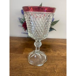 Peut inclure: Un gobelet vintage transparent avec un motif taillé en diamant sur le bol et un bord rouge. Le gobelet a une tige décorative et une large base festonnée. Le verre est transparent, laissant passer la lumière.