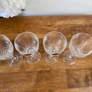 May include: Four clear glass stemmed drinking glasses with a diamond pattern. The glasses are arranged in a row on a wooden surface.