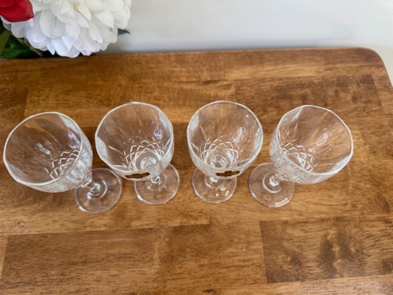 May include: Four clear glass stemmed drinking glasses with a diamond pattern. The glasses are arranged in a row on a wooden surface.