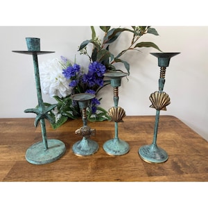 Könnte beinhalten: Vier dekorative teal Kerzenhalter mit maritimen Designs. Einer hat einen Seestern, ein anderer einen Fisch und zwei mit Muschelakzenten. Die Kerzenhalter aus Metall haben ein verwittertes Aussehen mit goldenen Akzenten.