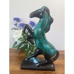 Peut inclure: Figurine de cheval en céramique, cabré. Le cheval a un corps vert-émeraude brillant et des pattes, une crinière et une queue noires. La figurine est montée sur une base noire et est un objet décoratif.