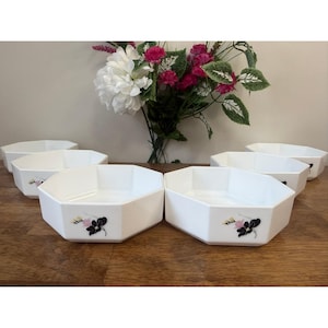 Peut inclure: Six bols de service blancs, octogonaux, avec un motif floral. Chaque bol présente un motif floral noir et rose. Les bols sont disposés sur une surface en bois, avec un bouquet de fleurs en arrière-plan.
