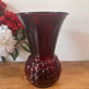 May include: A claret-coloured glass vase featuring a textured base and a flared opening. The vase is displayed with red and white flowers, suitable for home decoration. The vase's height is approximately 20 cm.