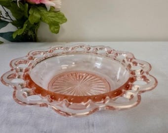 Pode incluir: Uma tigela de vidro rosa com uma borda festonada e um design delicado e rendado. A tigela tem um centro transparente e uma borda rosa.