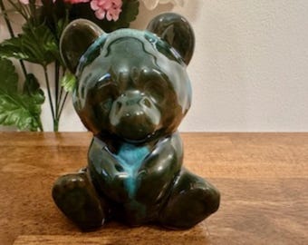 May include: A ceramic bear figurine with a dark green and teal glaze. The bear is sitting with its paws tucked in front of it.