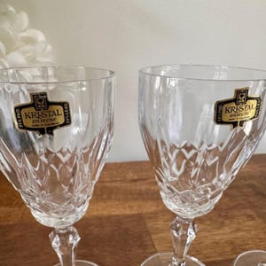 May include: Set of four clear glass wine glasses with a cut crystal design. Each glass has a gold label that reads "Kristal Zaječar".