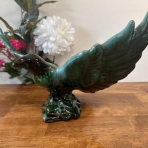 May include: A green glazed ceramic eagle figurine with outstretched wings. The eagle is perched on a green base.