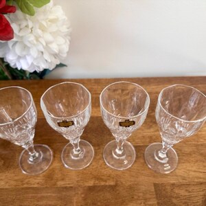 May include: Four clear glass shot glasses with a cut glass design. The glasses are arranged in a row on a wooden surface.