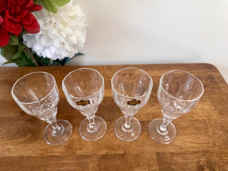 May include: Four clear glass shot glasses with a cut glass design. The glasses are arranged in a row on a wooden surface.