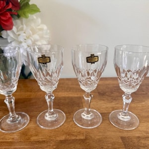 May include: Set of four clear glass stemmed shot glasses with a diamond pattern. Each glass has a gold label with the text "Bohemia Crystal" on it.