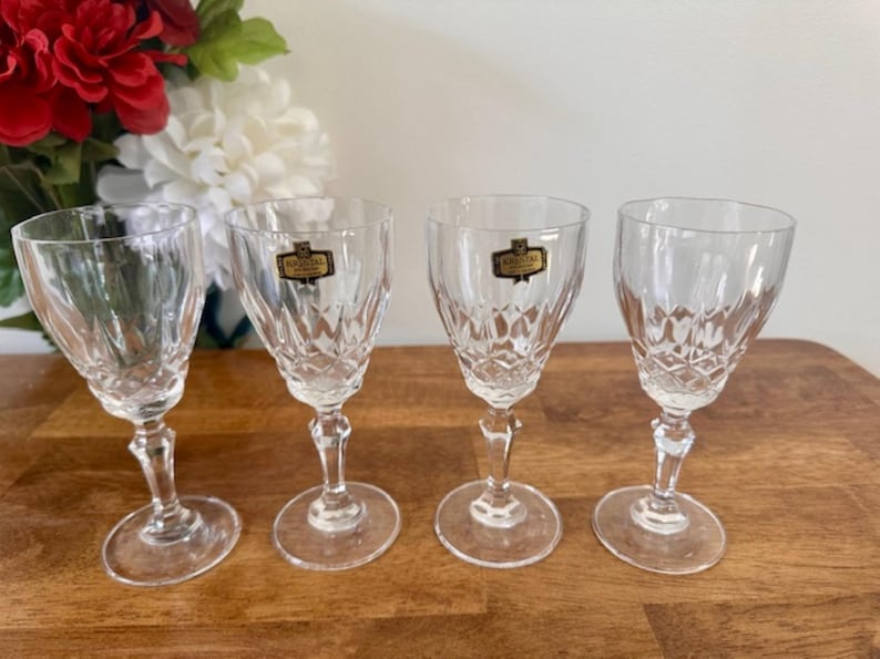 May include: Set of four clear glass stemmed shot glasses with a diamond pattern. Each glass has a gold label with the text "Bohemia Crystal" on it.