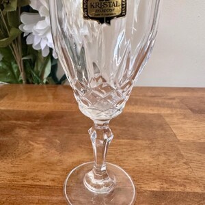 May include: A clear glass wine glass with a cut crystal design. The glass has a label that reads "KRISTAL Zaječar 24% PbO 24% Lead".