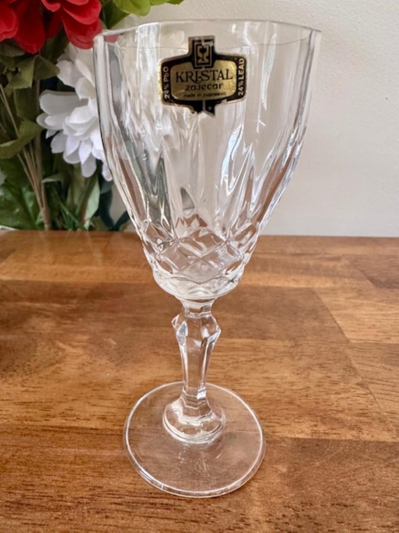 May include: A clear glass wine glass with a cut crystal design. The glass has a label that reads "KRISTAL Zaječar 24% PbO 24% Lead".