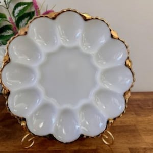 Peut inclure: Plat à œufs en verre laiteux blanc avec un bord doré. La plaque comporte 12 indentations individuelles pour contenir des œufs.