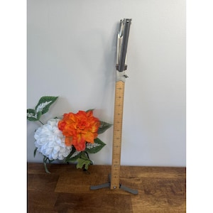 May include: A vintage metal and wood measuring tool with a folding ruler. The ruler is marked with inch increments. The tool has a metal base and a metal top with a folding mechanism. The ruler extends to 48 cm.