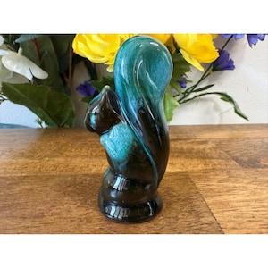 Op de afbeelding: Een keramieken eekhoornbeeldje met een glanzende afwerking. De eekhoorn is voornamelijk bruin met turquoise en donkergroene accenten. Het beeldje staat rechtop met zijn staart over zijn rug gebogen. De basis is donkerbruin.