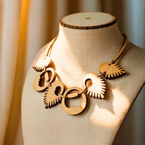 Op de afbeelding: Een houten ketting met bladvormige en cirkelvormige hangers. De ketting wordt op een mannequin getoond. De hangers zijn lichtbruin met donkerbruine accenten. De ketting is verbonden door een dun, lichtbruin koord.