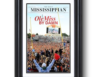 May include: Framed print of The Daily Mississippian newspaper cover, featuring a crowd celebrating at a football game. The headline reads "Ole Miss by Damn." The image is set in a black frame.