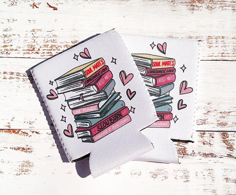 May include: Two white beverage insulators with pink hearts and stars. The insulators feature a stack of books with the text "Soul Mates", "Forbidden Love", "Fated Mates", "Love, Actually", "Slow Burn", and "Make Me Burn Like You" on the covers.