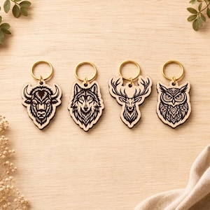 May include: Four wooden keychains featuring laser-engraved animal designs including a bison, a wolf, a deer with antlers, and an owl. Each light-colored wooden cutout is attached to a circular gold-toned metal split ring for keys.