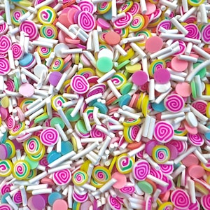 Peut inclure: Gros plan sur un assortiment coloré de décorations en pâte polymère. Le mélange comprend des bonbons tourbillons roses et blancs, des cercles aux couleurs pastel et des bâtonnets blancs rectangulaires. Les décorations sont éparpillées, créant une texture vibrante et ludique.