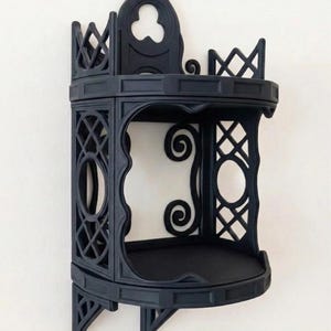 May include: A black, gothic-style corner shelf with intricate geometric and scrollwork details. The shelf has a rounded base and a decorative top with a trefoil design. The text "CLASSIC OBSIDIAN" is printed at the bottom.