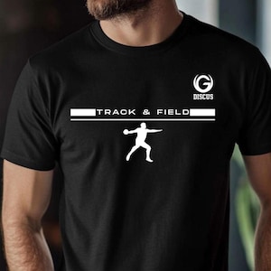 May include: Black t-shirt with a white graphic of a discus thrower and the words "TRACK & FIELD". Above the text is the word "DISCUS" and a stylized "G" logo. The shirt is a crew neck.