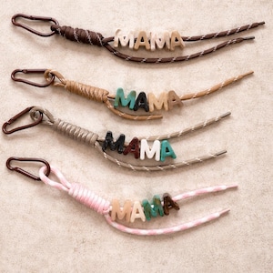 May include: Four keychains with the word "MAMA" spelled out in wooden beads. Each keychain has a different color scheme, including brown, tan, gray, and pink, with coordinating cord and a metal clasp.