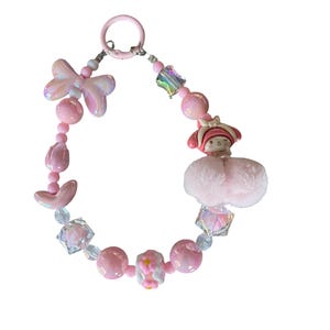 Pu&ograve; includere: Un portachiavi rosa con perline con una variet&agrave; di perline, tra cui perline iridescenti a forma di fiocco, perline di cristallo sfaccettate e perline rosa rotonde. &Egrave; incluso anche un piccolo personaggio rosa con un cappello rosso e un soffice pompon rosa.