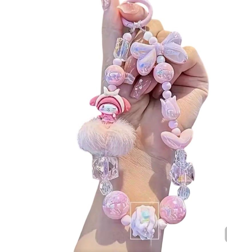 Pu&ograve; includere: Un portachiavi rosa con una variet&agrave; di elementi decorativi. Presenta un personaggio dei cartoni animati, un soffice pompon, perline iridescenti, un fiocco e accenti a forma di cuore. Il portachiavi &egrave; tenuto da una persona.