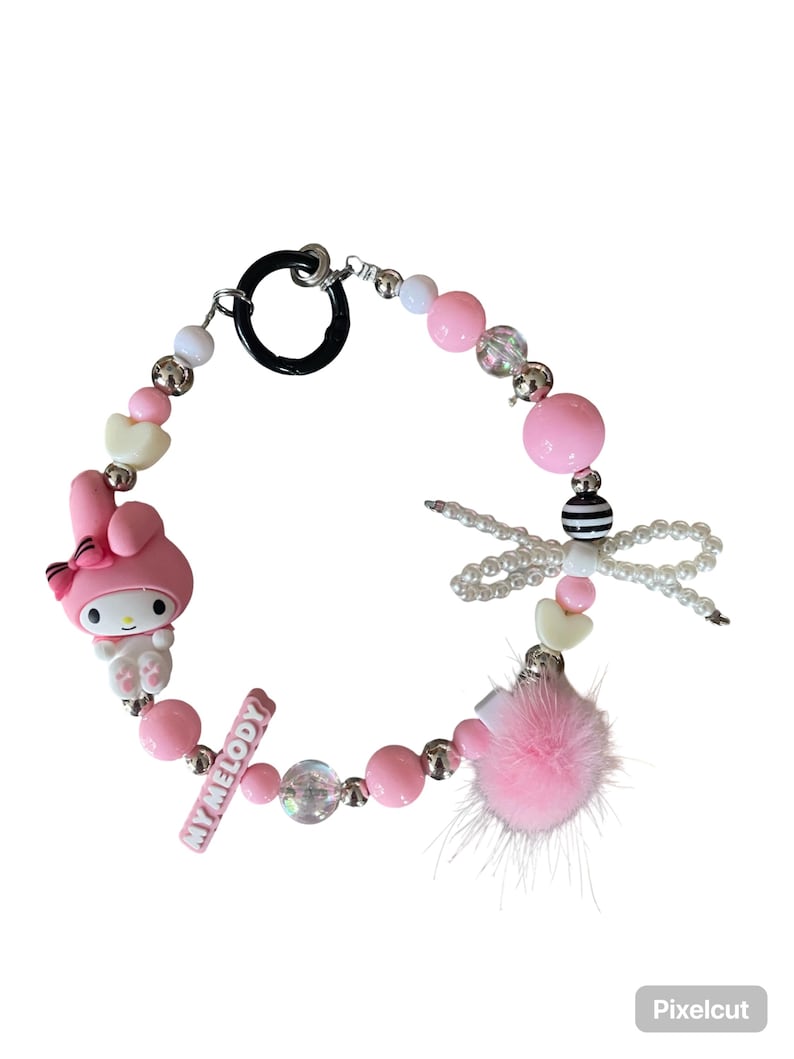 Pu&ograve; includere: Un braccialetto di perline rosa con un ciondolo My Melody, perline a forma di cuore e un pompon rosa. Il braccialetto include un ciondolo a forma di libellula e una barra con la scritta "MY MELODY". Il braccialetto ha una chiusura nera.
