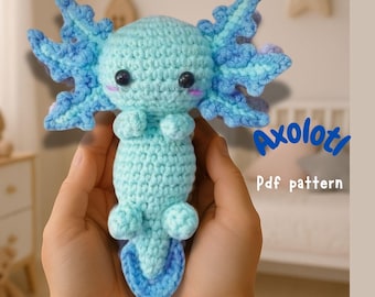 May include: A crocheted blue and light blue axolotl amigurumi toy. The axolotl is holding its arms in front of it and has a small tail. The toy is being held in a person's hands. The text "Axolotl Pdf pattern" is in the background.