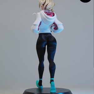 K&ouml;nnte beinhalten: Figur einer weiblichen Figur, von hinten gesehen, mit einem wei&szlig;en Kapuzenpullover mit einem roten und rosa Spinnennetz-Design, schwarzen Leggings und t&uuml;rkisfarbenen Schuhen. Die Figur steht auf einem schwarzen kreisf&ouml;rmigen Sockel. Das Logo "E.S.M" ist sichtbar.