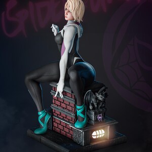 May include: A detailed figurine of a character in a black, white, and purple bodysuit, seated on a brick structure. The figure has blonde hair and teal high heels. The background features the words "SPIDER GWEN" in a purple graffiti style.