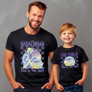 A man and a young boy wearing matching black t-shirts with the text "The Dadorian This is the Way" printed on them.