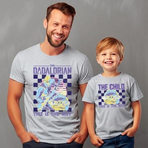 A man and a young boy wearing matching t-shirts with a graphic design featuring a character from the Star Wars franchise.