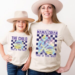 A woman and a child wearing matching t-shirts with a graphic design related to the Star Wars series "The Mandalorian".