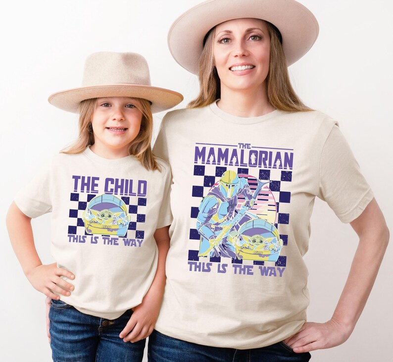 A woman and a child wearing matching t-shirts with a graphic design related to the Star Wars series "The Mandalorian".