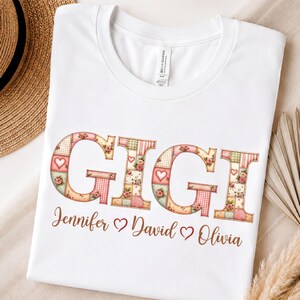 Könnte beinhalten: Ein weißes Kurzarm-T-Shirt mit dem Wort GIGI in großen Buchstaben im Patchwork-Stil, verziert mit Blumen-, Herz- und Karomustern in Rosa, Grün und Creme. Darunter sind die Namen Jennifer, David und Olivia in brauner Schrift aufgedruckt.