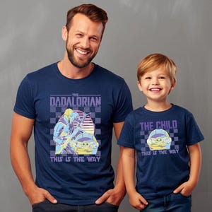 A man and a young boy wearing matching blue t-shirts with a graphic design.