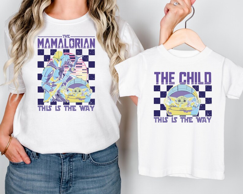 A woman wearing a white t-shirt with a graphic design featuring a character from the Star Wars series, The Mandalorian, and a child wearing a smaller t-shirt with the same design.