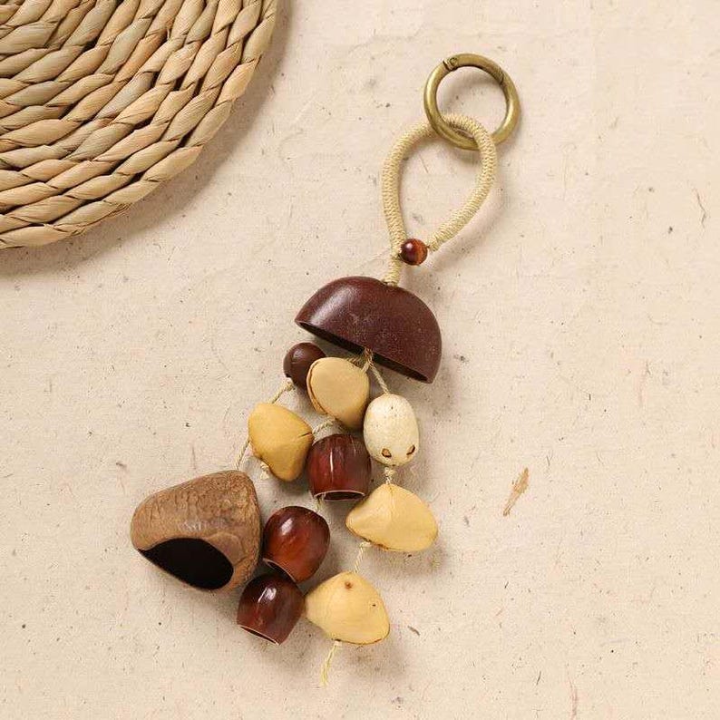 May include: A handcrafted keychain featuring a collection of natural, organic elements. The keychain includes a dark brown, half-dome shape, various seed pods, and small, rounded wooden beads. A brass ring and beige cord complete the design.