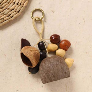 May include: A handmade keychain featuring a collection of natural elements. It includes a variety of wooden beads, dark brown seeds, and a large, textured, light brown stone. The keychain is attached to a gold-colored ring.