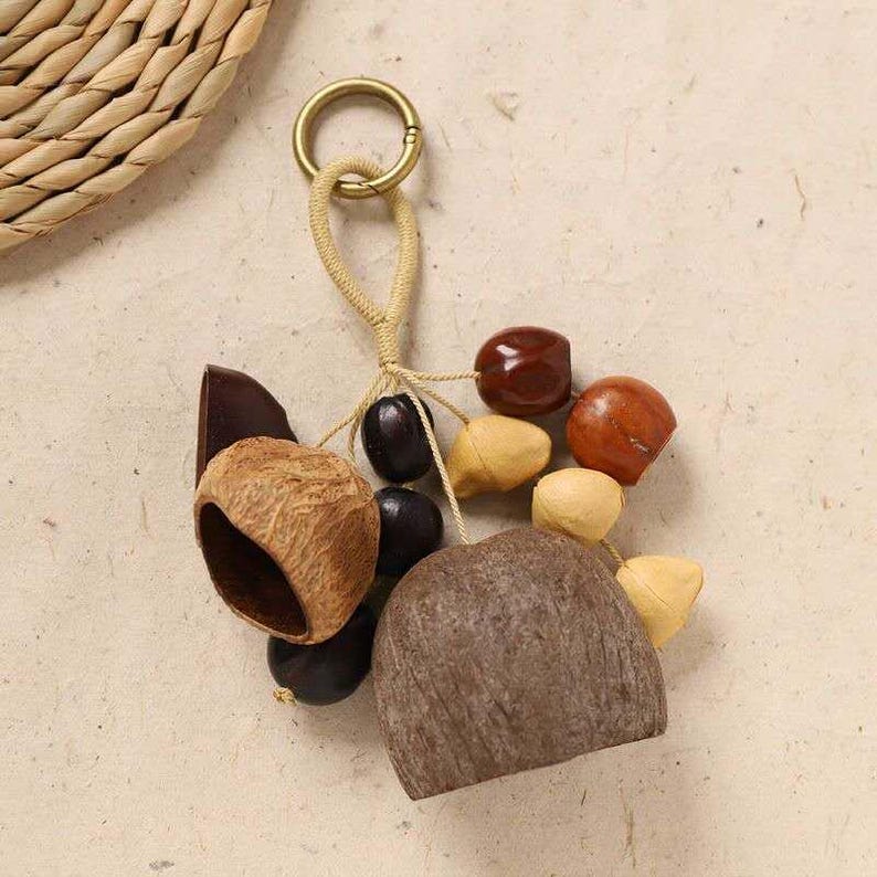 May include: A handmade keychain featuring a collection of natural elements. It includes a variety of wooden beads, dark brown seeds, and a large, textured, light brown stone. The keychain is attached to a gold-colored ring.